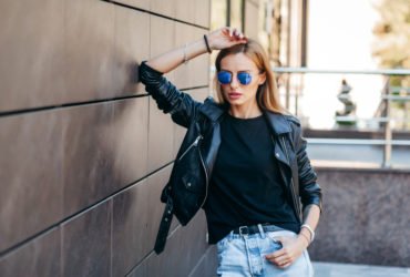 Girl wearing black t-shirt, glasses and leather jacket posing ag